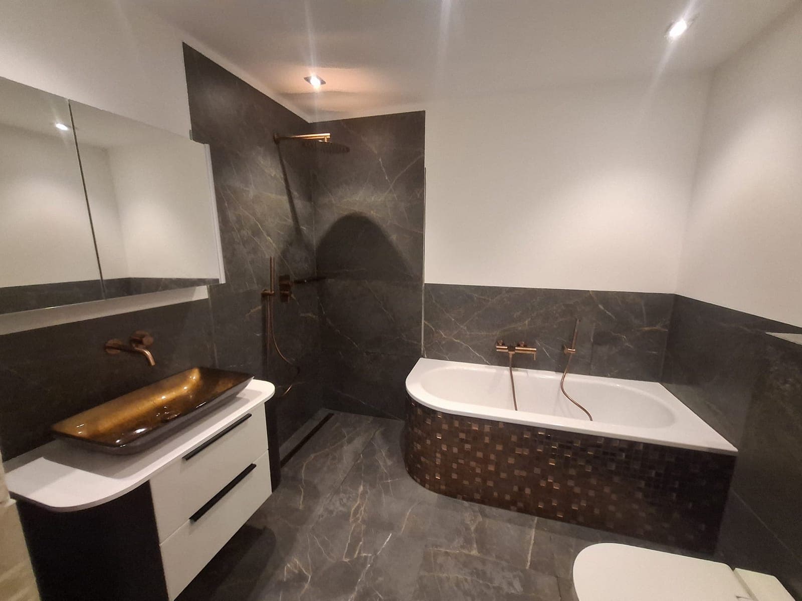 Badezimmer mit goldenem Aufsatzbecken und Badewanne in dunkler Steinoptik